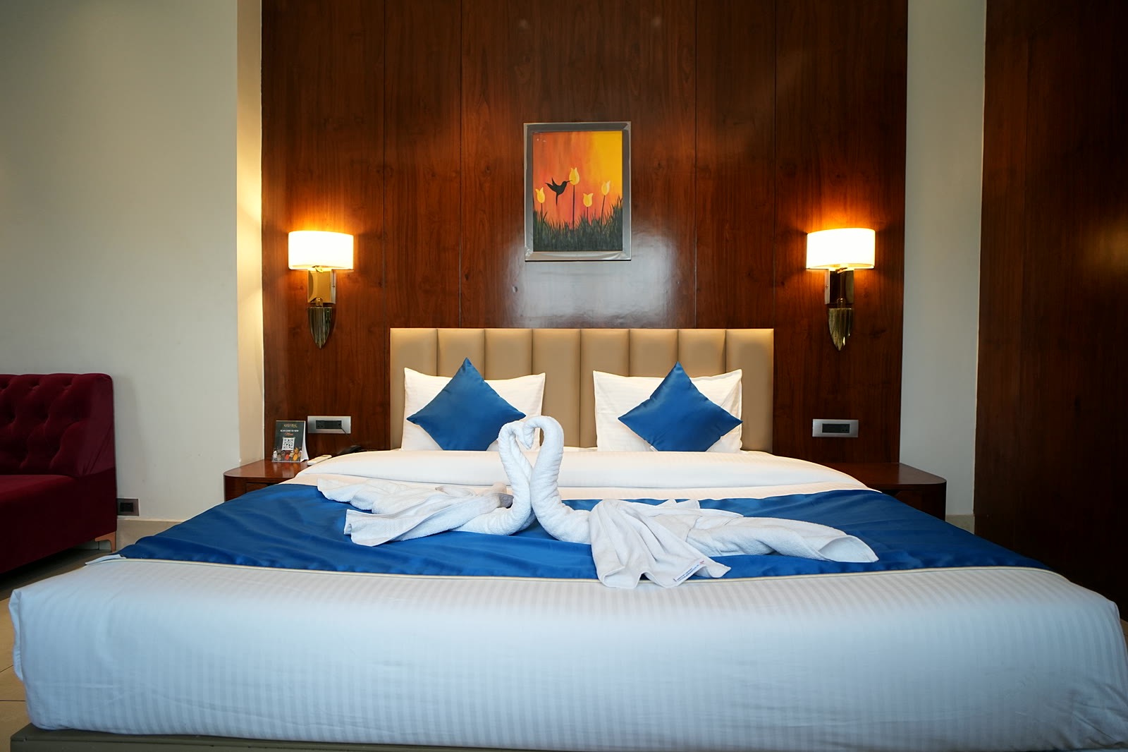 A bed made up with blue runner and cushions, wood-panelled wall and twin lamps