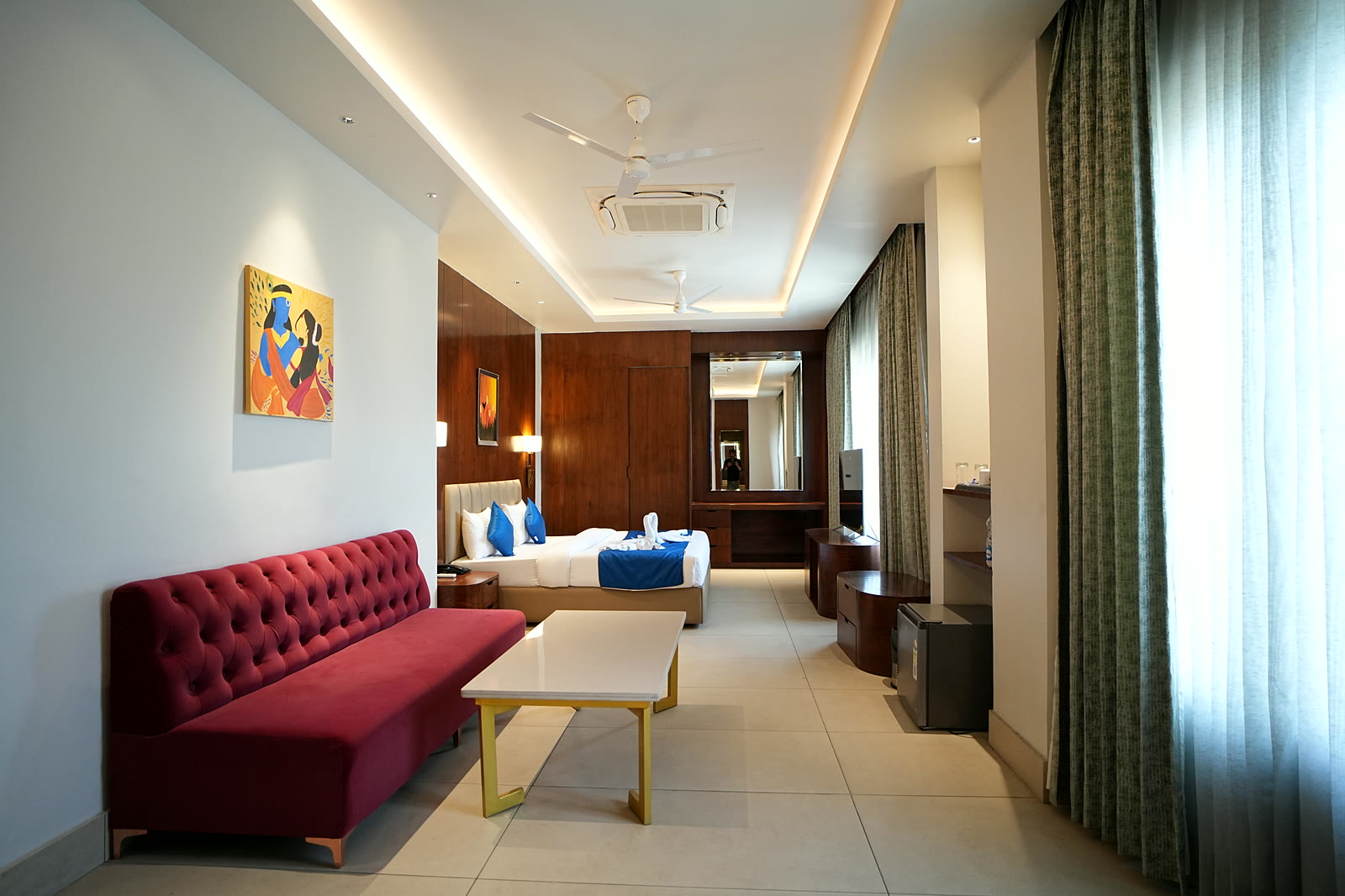 A long room with a red tufted sofa, a coffee table, and the bed beyond