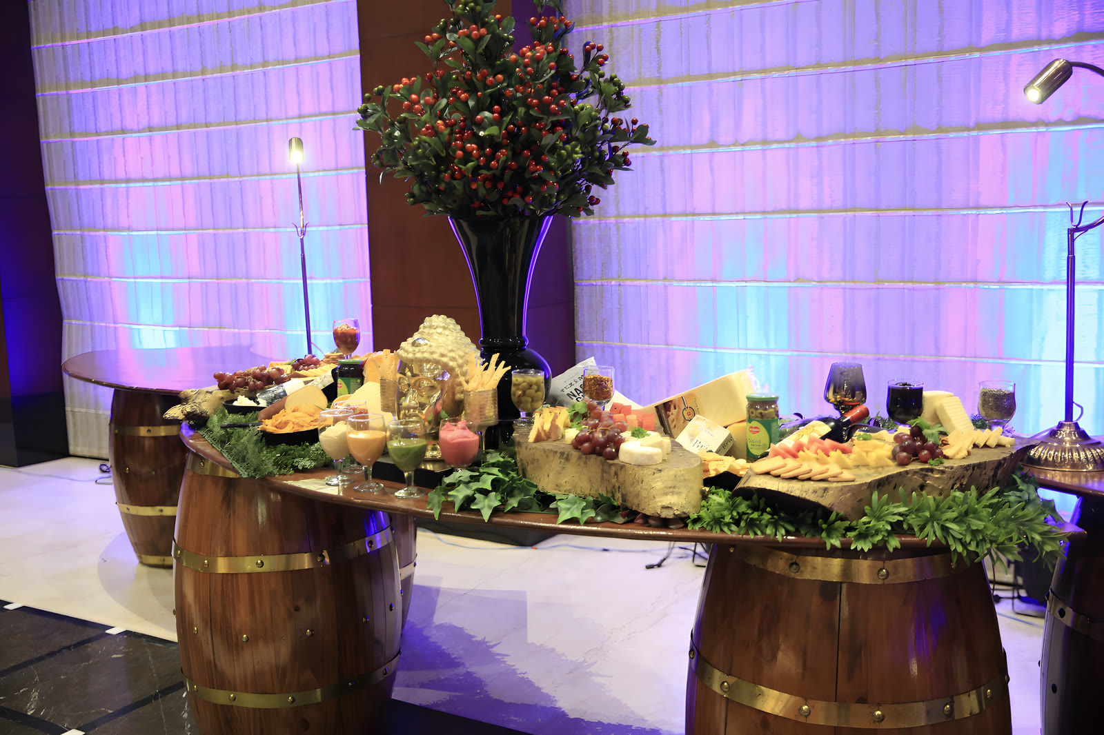 A grazing table of cheeses, fruit and breads laid on oak barrels, under violet light
