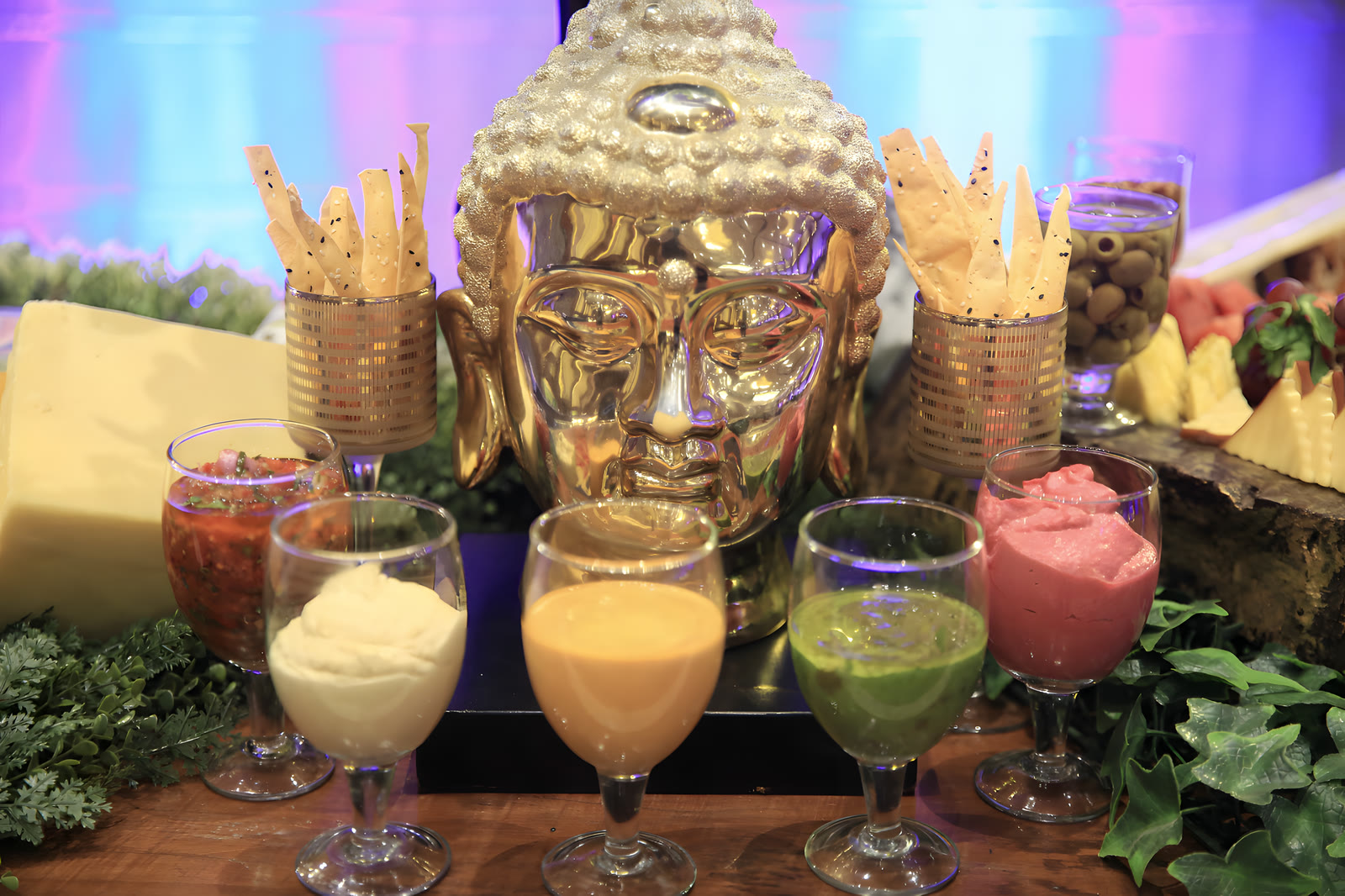 Glasses of coloured shakes and mocktails around a gold Buddha head, with crisps in brass cups